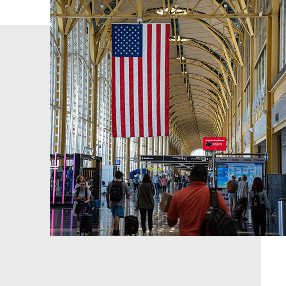 Travelers at airport with large American flag overhead.